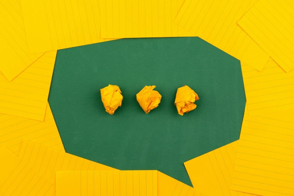 orange sheets of paper lie on a green school board and form a chat bubble with three crumpled papers.